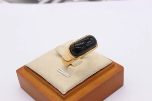 Macro detail of a wide gold-plated ring featuring a polished rectangular black gemstone