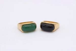 Close-up of gold-plated saddle rings with emerald green and black onyx-style gemstones