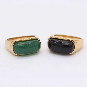 Gold-plated rings with rectangular emerald green and black gemstones on a gray background