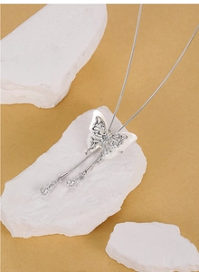 Macro detail of silver butterfly pendant with white shell wings and double tassels