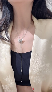 Detail of S925 silver butterfly pendant on a long Y-shaped necklace over a suit