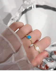 Detalle de anillos de ópalo con bandas doradas trenzadas y piedras laterales brillantes