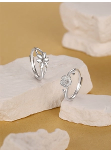 Détails des bagues lys et fleurs de cerisier en argent S925 sur un socle en pierre blanche