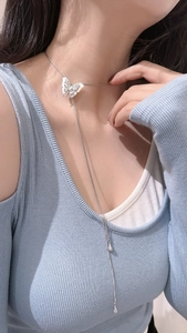 Macro detail of silver butterfly pendant with long tassel chain on blue knit sweater