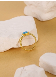 Detalle de un anillo dorado trenzado con ópalo azul ovalado y pequeños circones finos