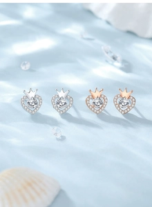 Macro shot of silver and rose gold heart crown stud earrings on blue silk background