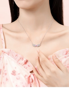 Close-up of angel wing necklace with a pink heart pendant worn on the neck