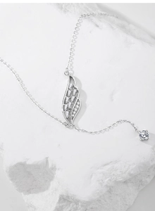 Dettaglio della collana con ali in argento S925 e zirconi su sfondo di pietra