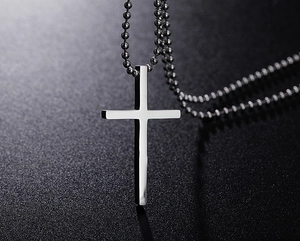 Polished silver cross pendant on bead chain against a textured grey background