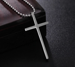 Polished silver cross pendant on ball chain resting against a dark wood box