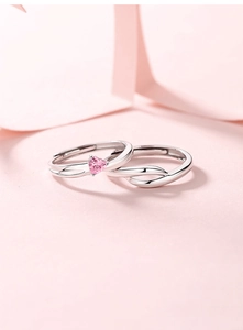 Detailed shot of open silver couple rings with a pink heart gemstone on a soft pink background