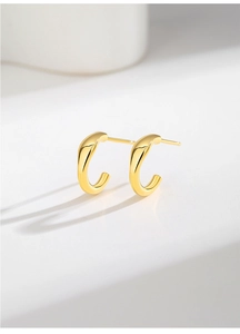 Gros plan sur des boucles d'oreilles clous dorées en C au design demi-cercle minimaliste