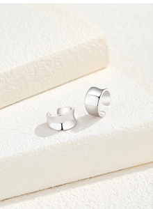 Detailed view of polished S925 silver ear cuffs on a white textured stone staircase