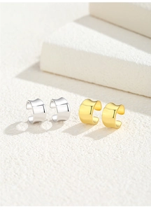 Macro detail of S925 silver and gold irregular C-shape ear cuffs on white textured backdrop