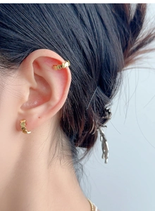 Détail macro d'un earcuff doré texturé vague et d'une boucle d'oreille assortie