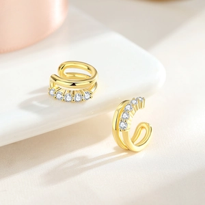 Double-layer gold ear cuff with small round zircons on a white minimalist pedestal