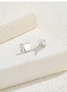 Macro shot of polished square silver stud earrings on a white stone background display