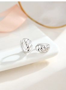 Détail de créoles en argent S925 torsadées avec texture brillante sur une assiette blanche