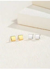 Detail showing gold and silver square mirror-finish studs on a white stone background
