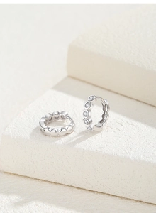 Detailed view of silver hoop earrings with round zircons on a white stone pedestal