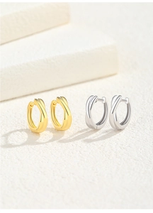 Close-up of interlocking gold and silver twisted hoop earrings on cream stone