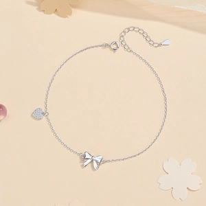 S925 sterling silver anklet with polished bow and pavé zircon heart charms on beige background