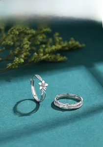 Dettaglio di anelli di coppia in argento S925 con motivi di fiori e viti su fondo verde