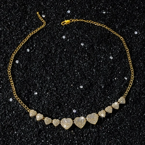 Macro shot of gold hip-hop necklace with iced-out heart pendants on black sand background