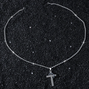 Gros plan du pendentif croix argenté avec prière gravée sur fond texturé noir