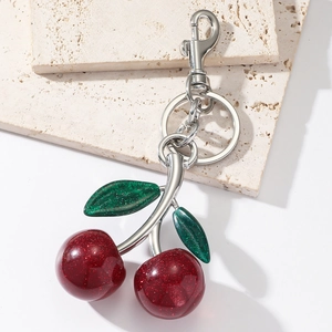Sparkly red cherry resin keychain with green glitter leaves on a stylish stone display
