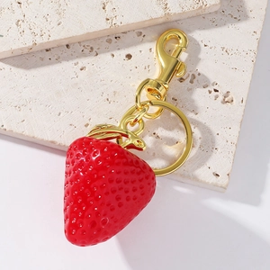 Macro view of realistic red strawberry keychain with gold hardware on travertine stone