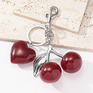 Sparkly red resin cherry heart keychain with silver metal clasp on a travertine stone