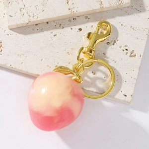 Close-up of peach fruit resin keychain with pink marble texture on stone base