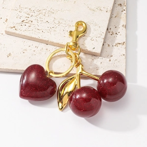Sparkly resin heart and cherry keychain charm with golden hardware on a stone base