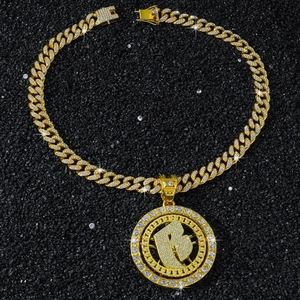 Macro shot of iced out rotating letter B pendant with gold Cuban link chain on dark stones
