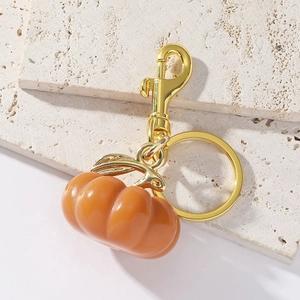 Close-up of bright orange resin pumpkin keychain with gold metal leaf on stone background