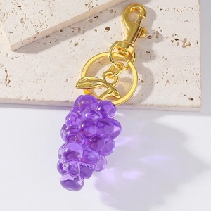 Macro detail of purple resin grape keychain with golden metal hook and leaf charm