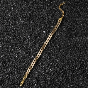Close-up of a gold-plated Cuban chain anklet with sparkling pavé zircons on black gravel