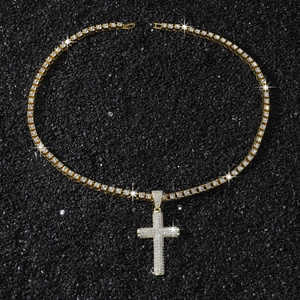 Detail of a gold plated iced out cross pendant with a tennis chain on black background