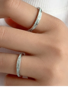Macro detail of silver rings with light blue wavy enamel inlay worn on finger