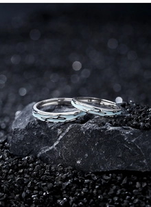 Close-up of luminous silver couple rings with light blue fluid texture on dark stone