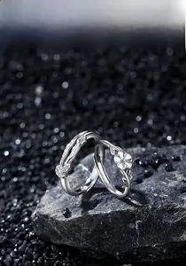 Detail of 925 sterling silver couple rings with camellia flower on dark stone background