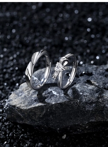 Detailaufnahme der S925 Silber-Partnerringe mit Schleife und Herzstein auf schwarzem Fels