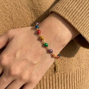 Colorful beaded bracelet with gold metal chain on wrist with warm brown sweater