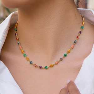 Detail shot of golden necklace with colorful shell pendants on a white shirt