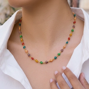 Close-up of a colorful baroque pearl necklace with gold chain worn on a white shirt