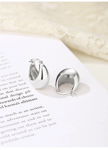 Close-up of teardrop silver hoop earrings with a polished mirror finish on white lace