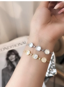 Detailed view of gold and silver S925 bracelets with square white shell pendants on wrist