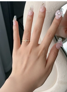 Nahaufnahme eines goldenen Kreuzrings mit Zirkonia an einer Hand mit Nagelkunst