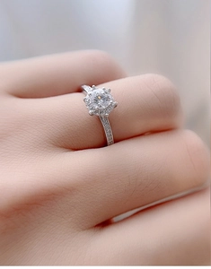 Close-up of a silver halo ring with six-prong setting and pavé diamonds worn on a finger